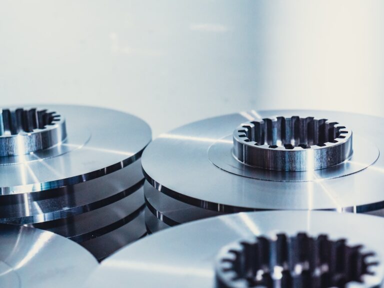 A worker operates a metal stamping press with sheets of metal stacked beside the machine.