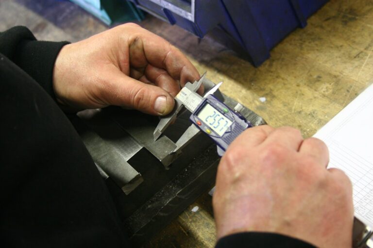 Technicians operate large stamping presses while forming metal components inside a well-lit industrial workshop.