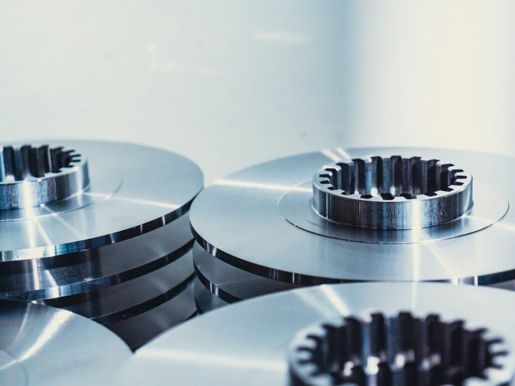 Technician measuring a stamped metal bracket beside a press with calipers and inspection gauges.