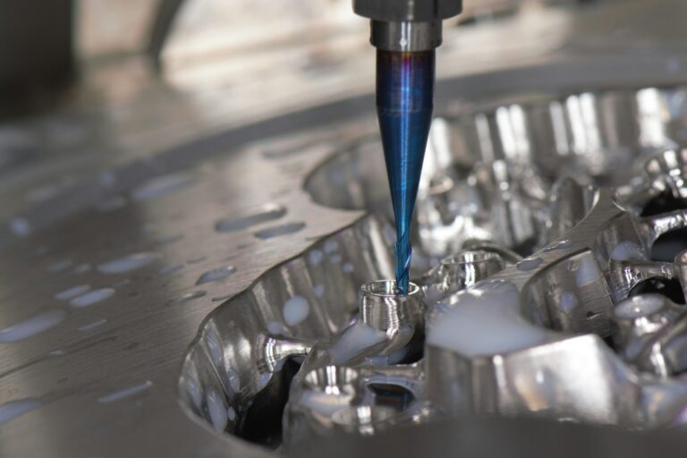 Machinist inspecting a steel stamping die beside a press with punches, plates, and formed sheet metal parts.