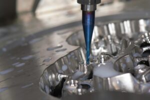 Engineer reviewing a 3D stamped metal part model beside a sheet metal die on a workstation.